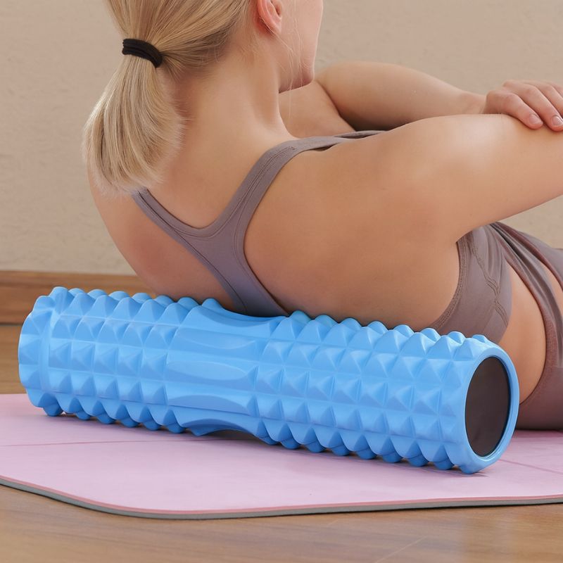 Femme blonde massant son dos avec un rouleau de massage bleu sur un tapis rose