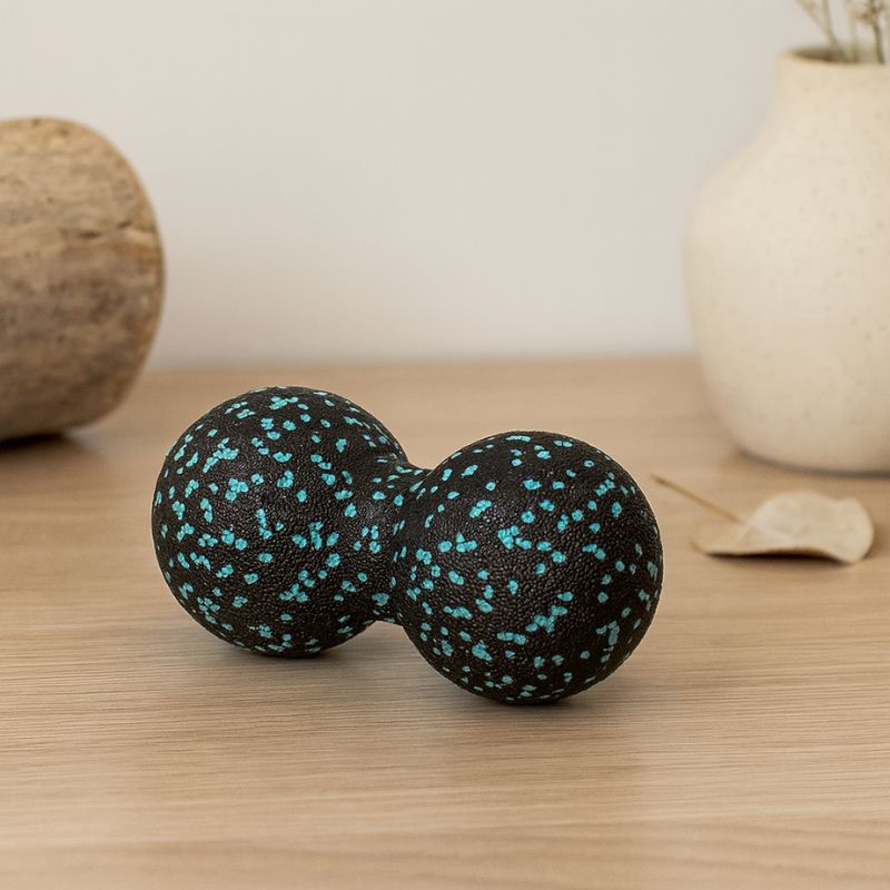 Balle de massage dos noire et bleue posée sur une table en bois dans un décor naturel