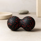 Balle de massage dos noire et rouge posée sur une surface minérale ambiance zen