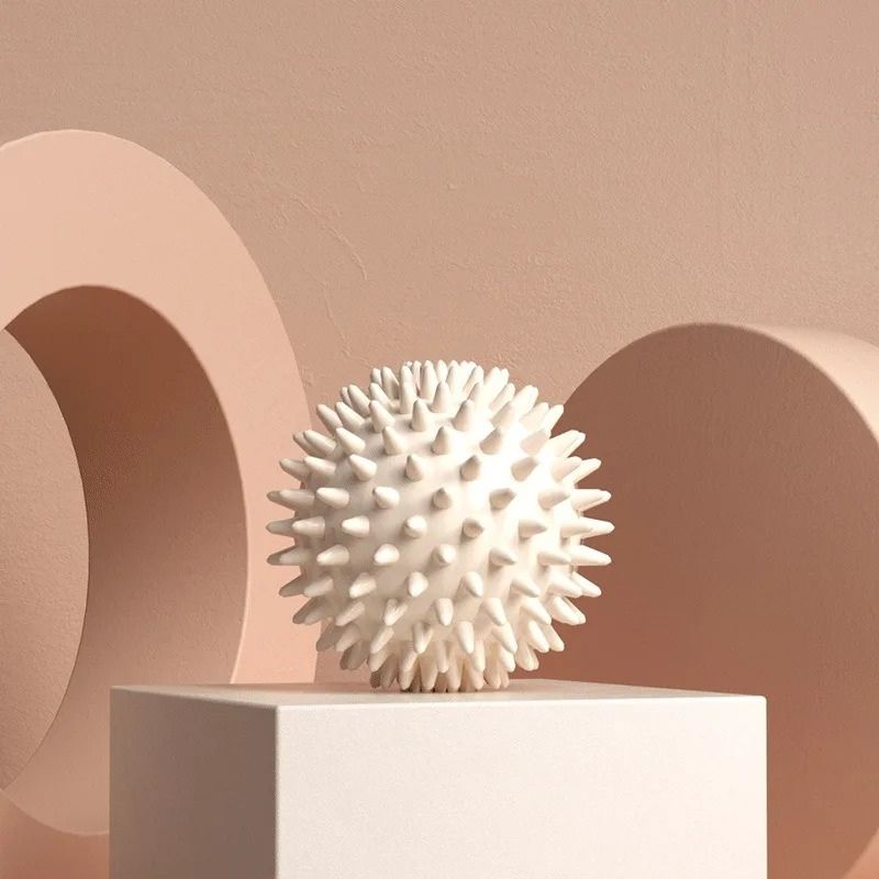 Balle de massage picots blanche posée sur un socle dans un décor minimaliste et zen