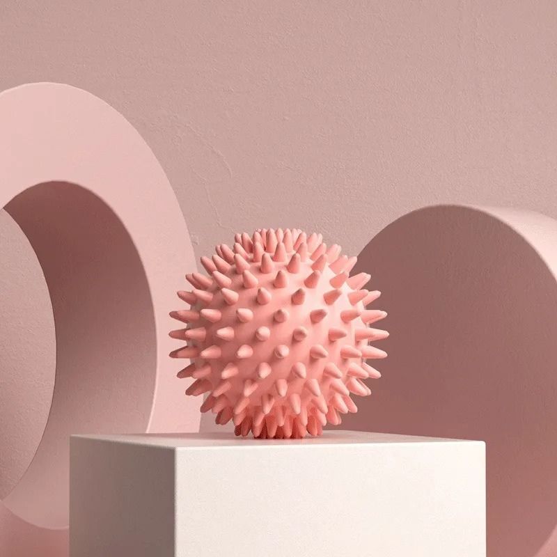 Balle de massage picots rose exposée sur un support clair avec ombres douces