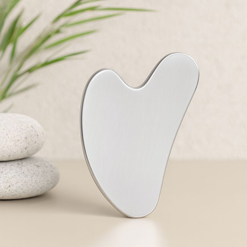 Gua Sha en acier inoxydable debout, accessoire de soin du visage dans une ambiance zen