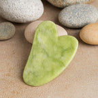 Gua Sha en jade vert sur des galets dans une ambiance zen et spa