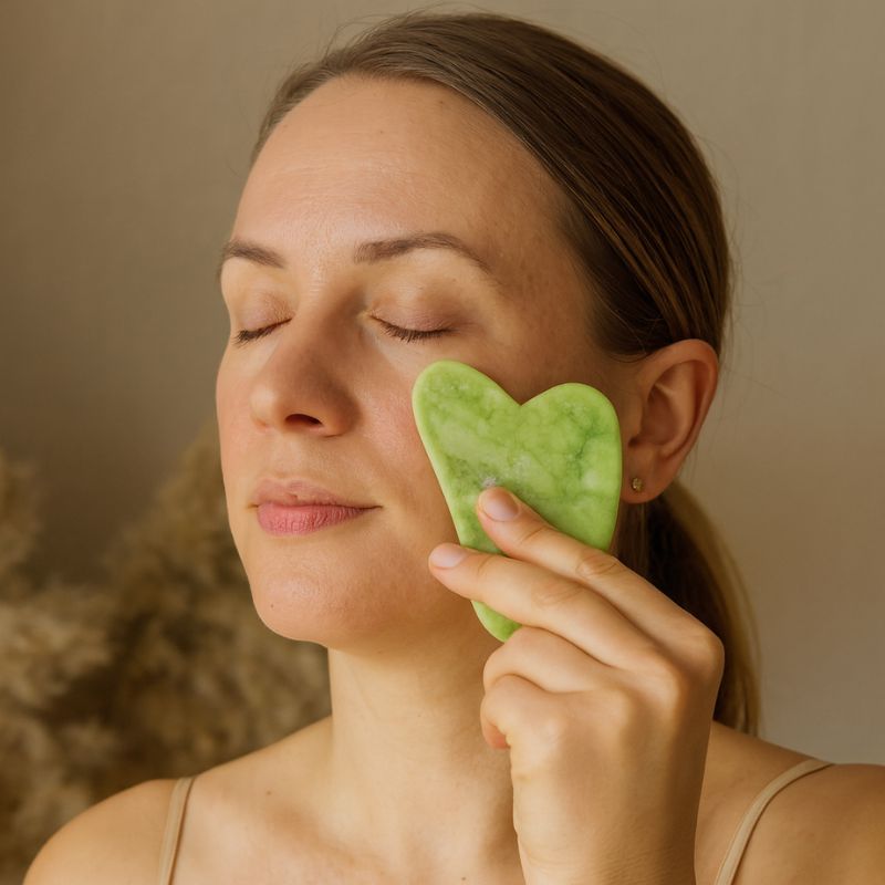 Femme utilisant un Gua Sha en jade pour masser sa joue, soin relaxant du visage