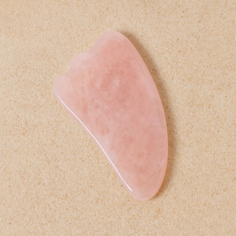 Gua Sha Quartz Rose posé sur pierre naturelle