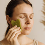 Femme utilisant une pierre Gua Sha en jade vert sur le visage dans une ambiance zen minimaliste