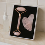 Kit massage visage quartz rose avec rouleau et pierre Gua Sha à côté d’un sérum pour massage facial
