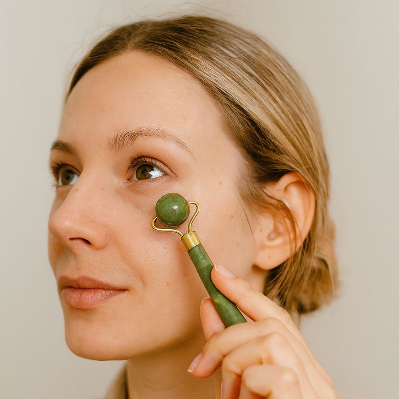 Jeune femme massant son visage avec un rouleau de jade boule pour stimuler la peau
