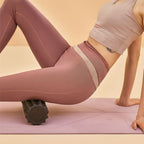 Femme utilisant un rouleau de massage dos noir sur tapis de yoga pour soulager ses muscles