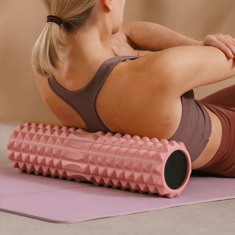 Femme s’étirant sur un rouleau de massage dos rose pour détendre le haut du dos