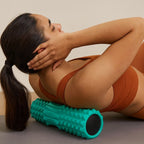  Femme sur tapis gris utilisant un rouleau de massage dos turquoise pour soulager ses tensions